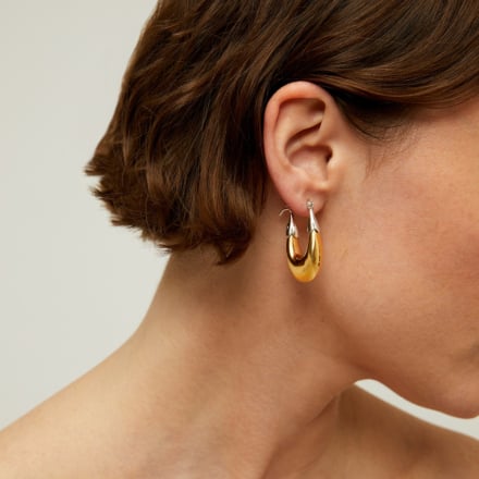 Gold hoop earrings worn by a woman with a neutral background