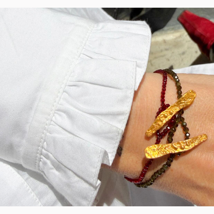 Close-up of a wrist wearing gold and red beaded bracelets with a white shirt background.
