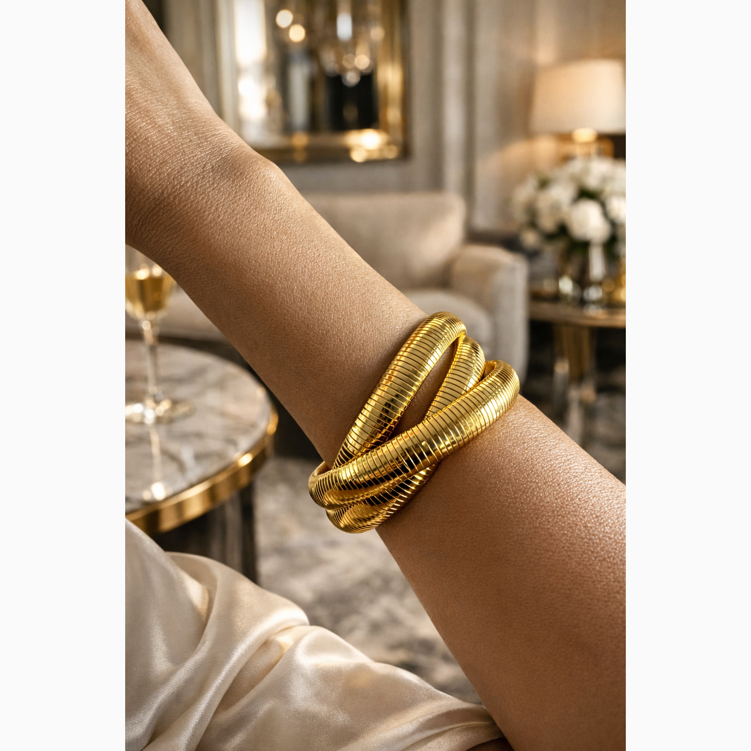 Gold bracelets on a person's wrist with a blurred elegant interior background