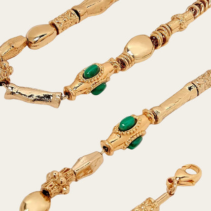 Gold necklace with green gemstones on a white background