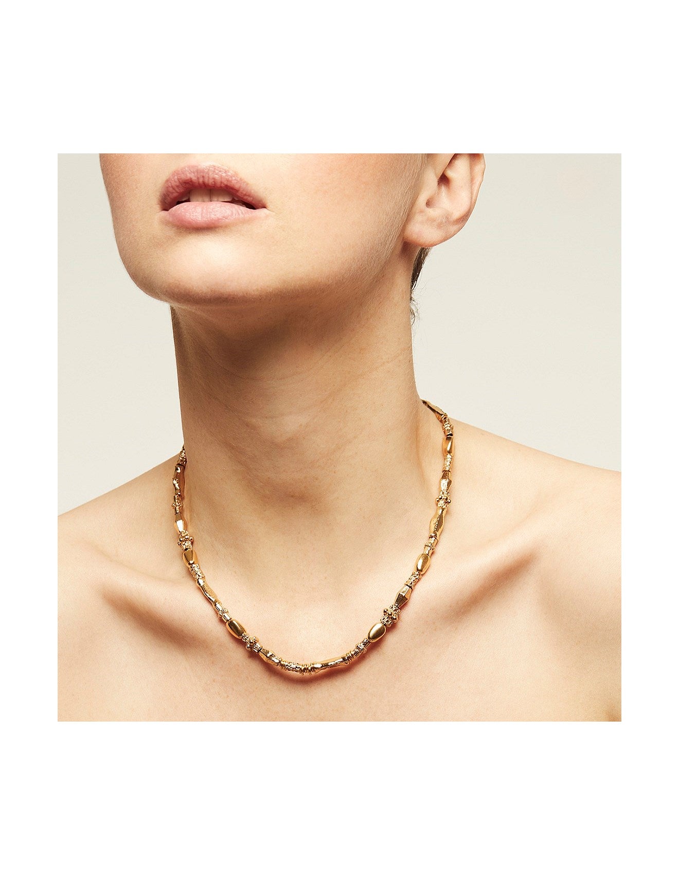 Gold chain necklace worn by a person on a neutral background