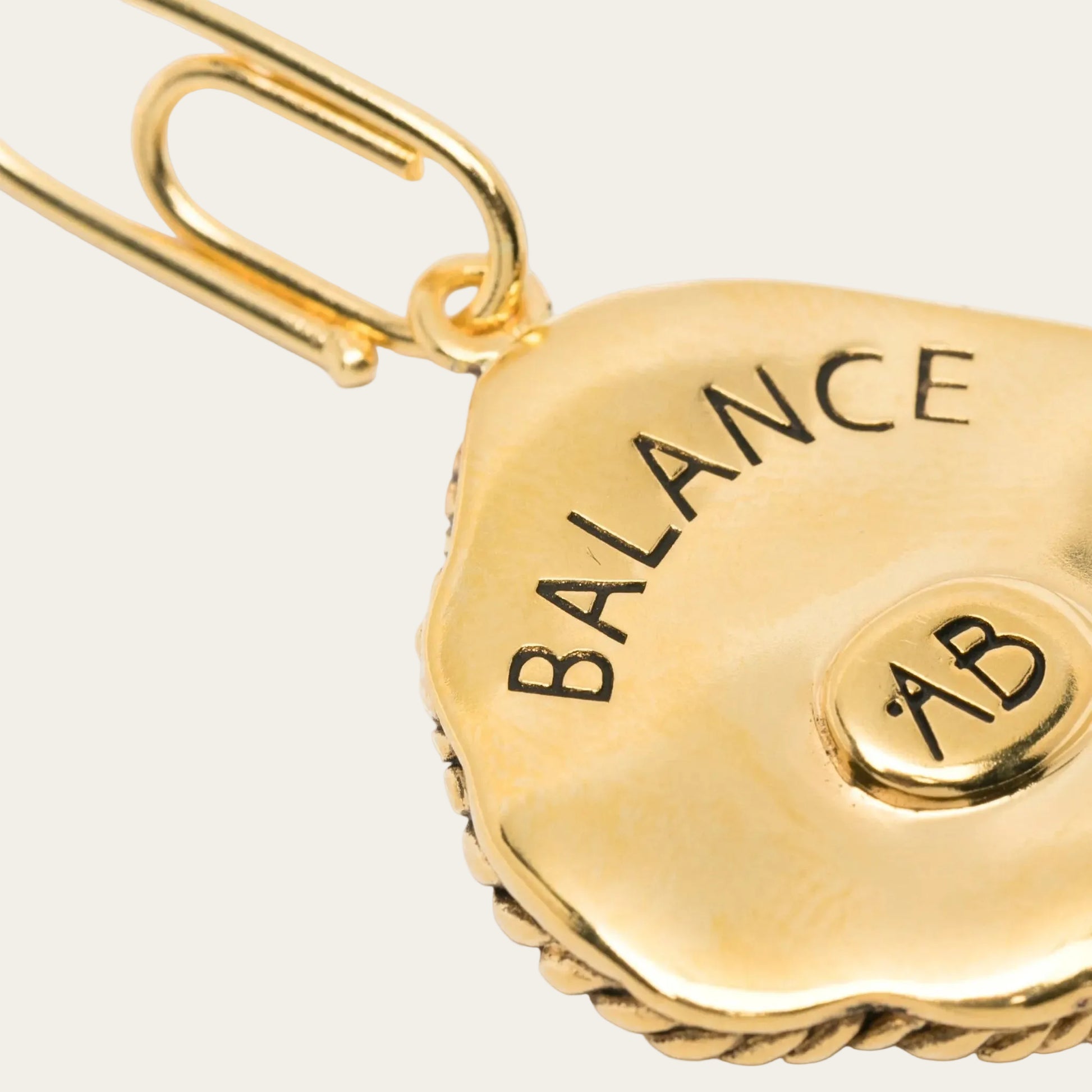 Gold charm with 'BALANCE AB' text on a white background