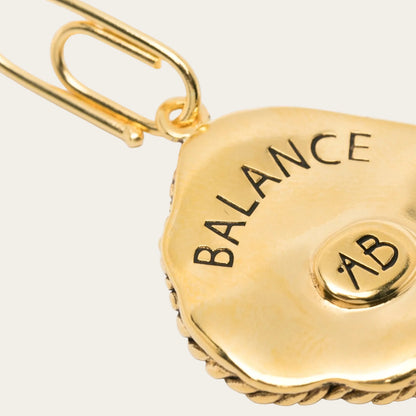 Gold charm with 'BALANCE AB' text on a white background