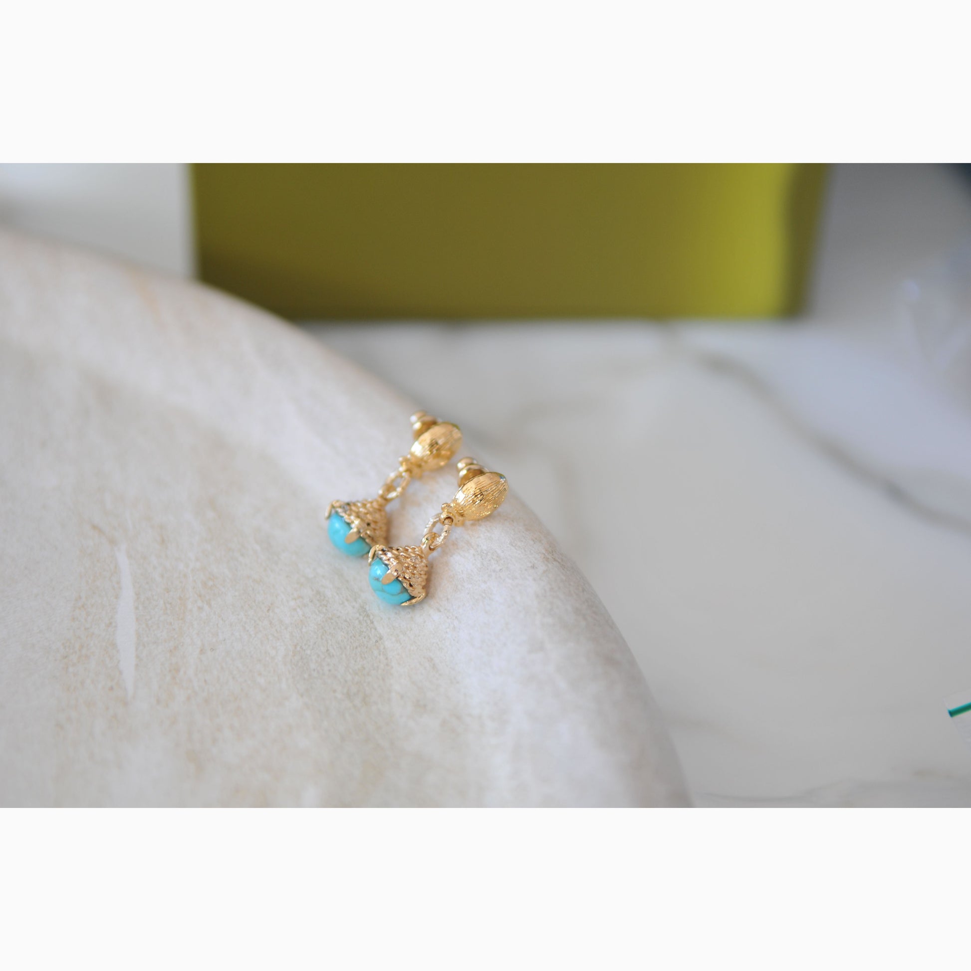 Gold earrings with turquoise stones on a white surface