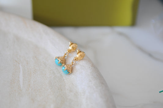 Gold earrings with turquoise stones on a white surface