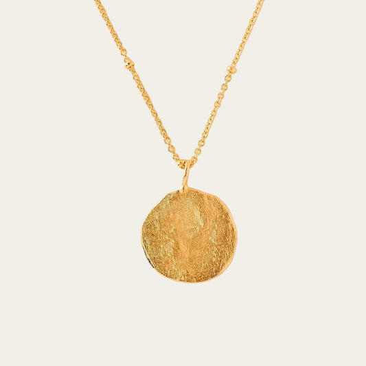 Gold necklace with a round pendant on a beige background