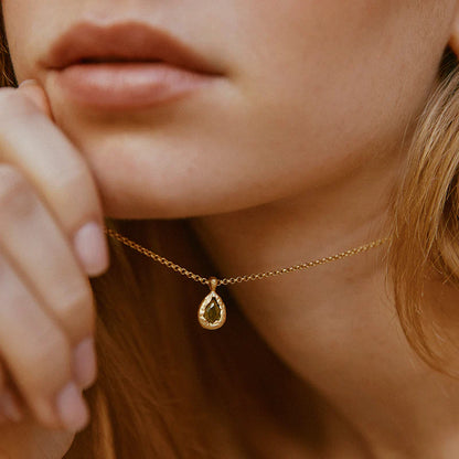 Close-up of a person wearing a gold necklace with a teardrop pendant.