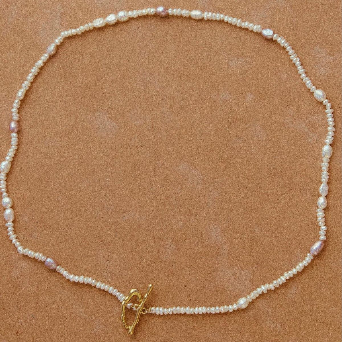 Pearl necklace with a gold clasp on a brown background