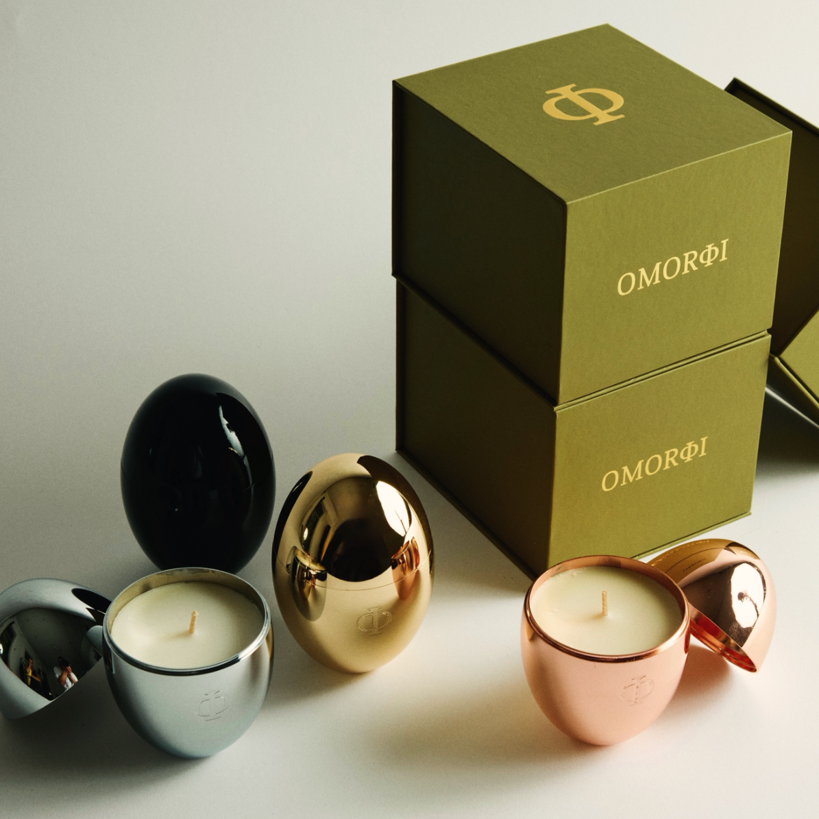 Set of candles in metallic holders with 'OMORFI' branding on a light background