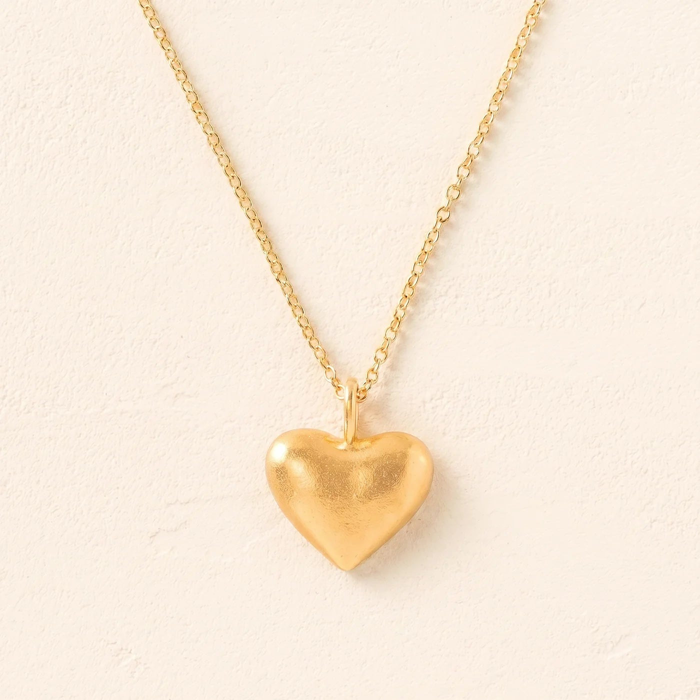 Gold heart-shaped pendant necklace on a beige background