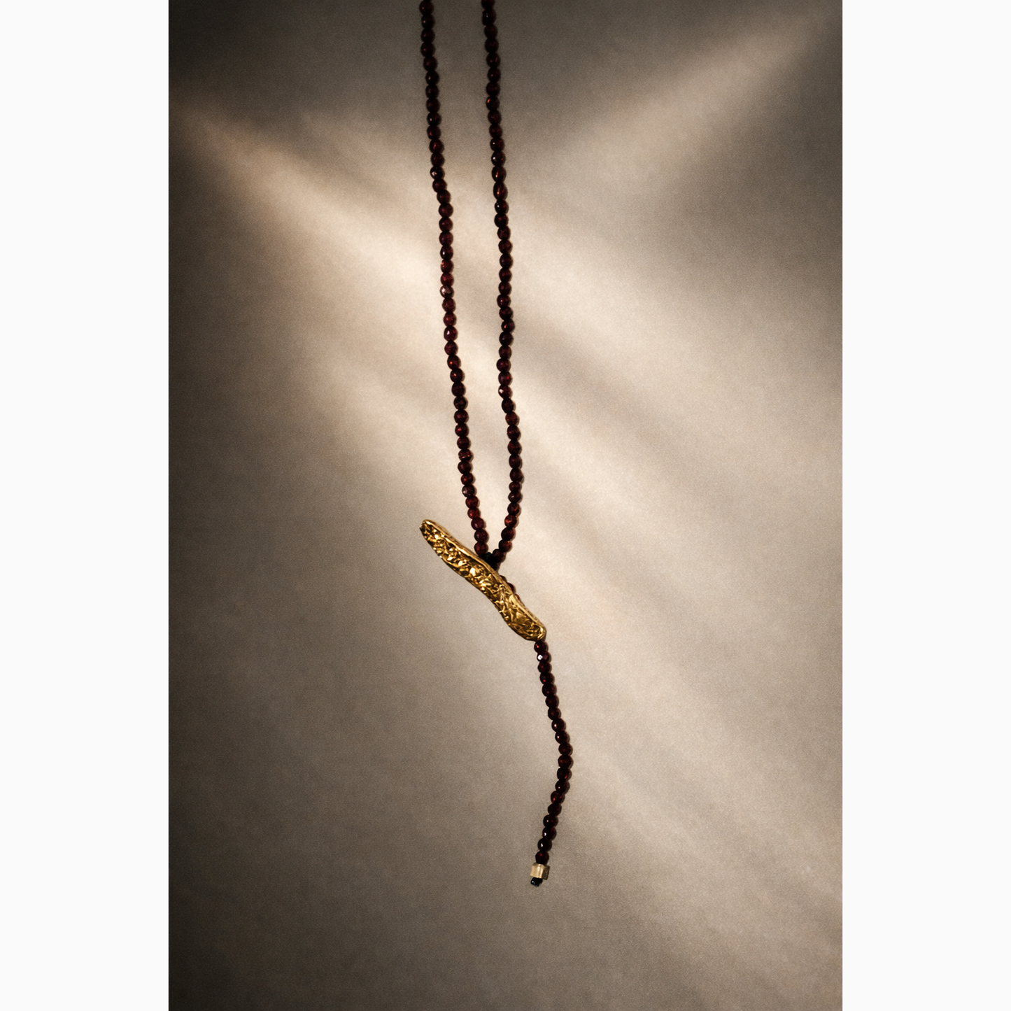 Necklace with dark beads and a gold clasp on a textured gray background