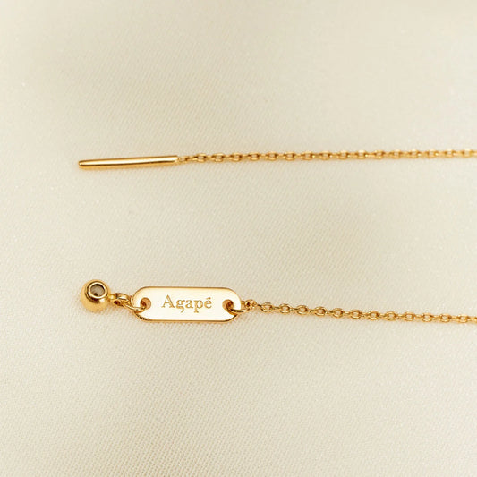 Gold necklace with a tag engraved 'Agapé' on a beige background