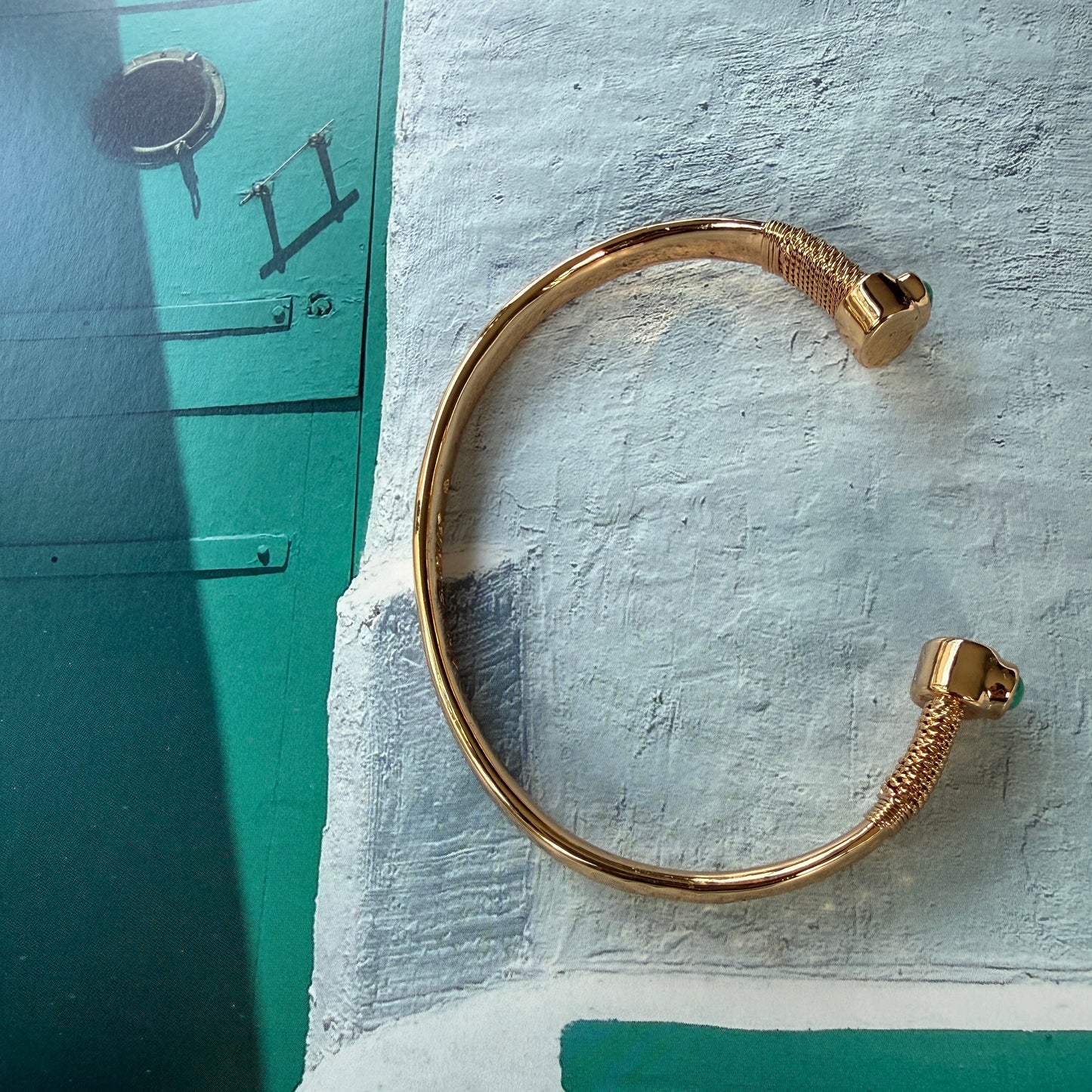 Gold bracelet on a textured surface with a cat in the background