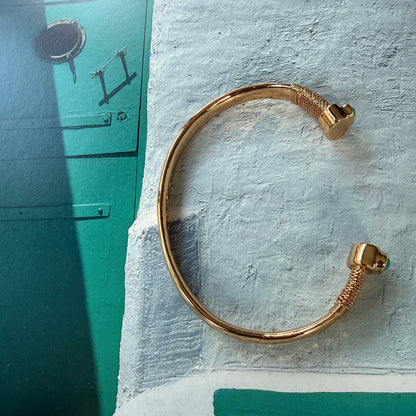 Gold bracelet on a textured surface with a cat in the background