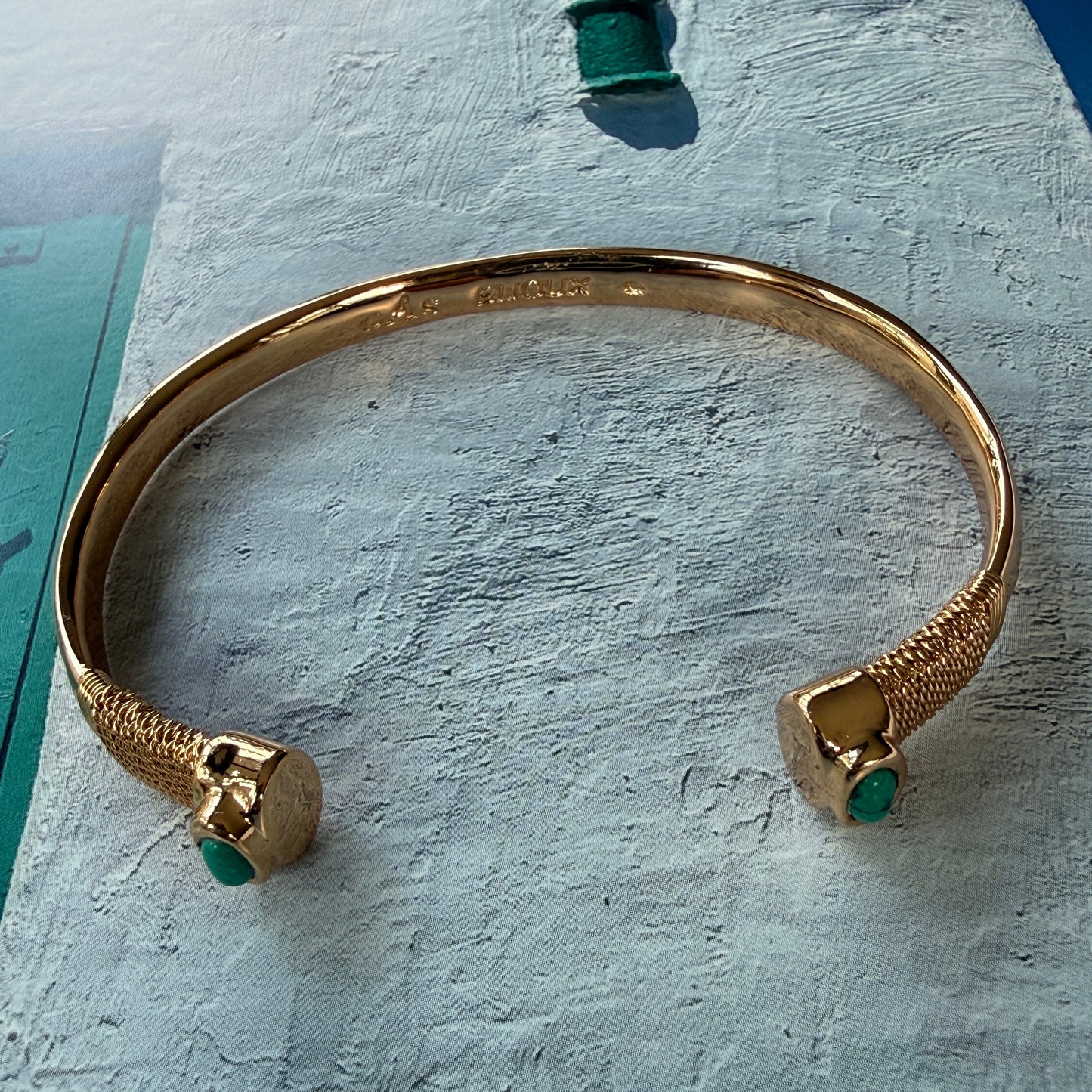 Gold bracelet with green stones on a textured surface