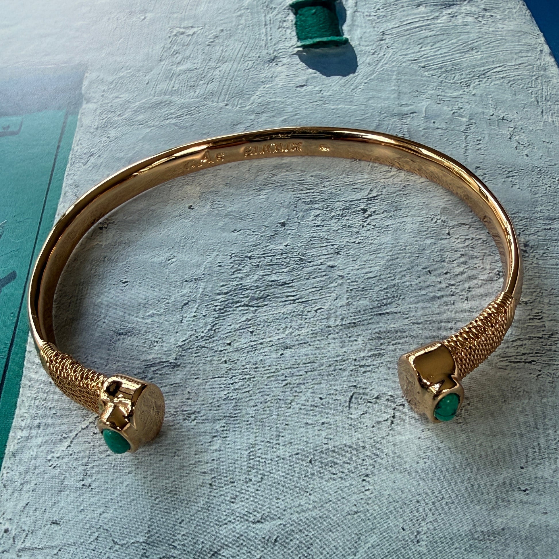 Gold bracelet with green stones on a textured surface