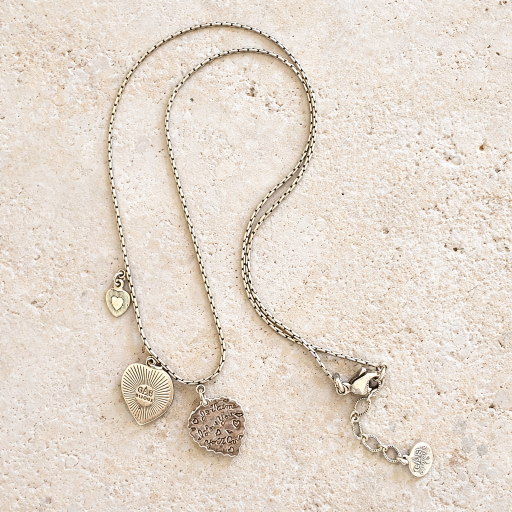 Silver necklace with heart-shaped pendants on a sandy surface