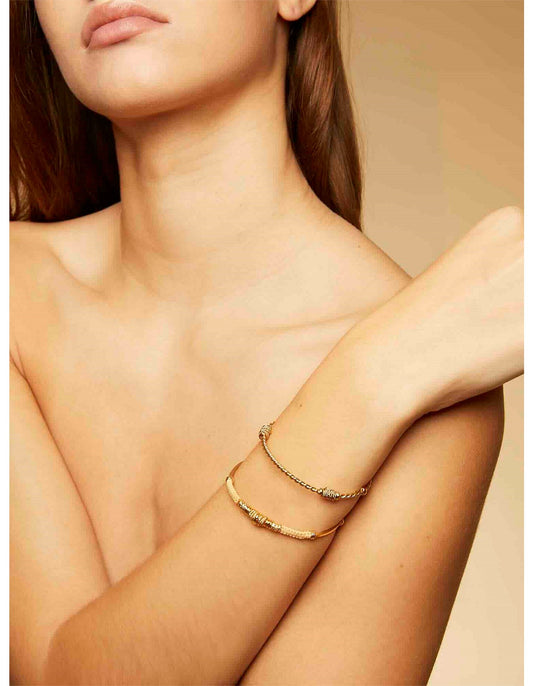 Close-up of a woman's arm wearing two gold bracelets on a beige background
