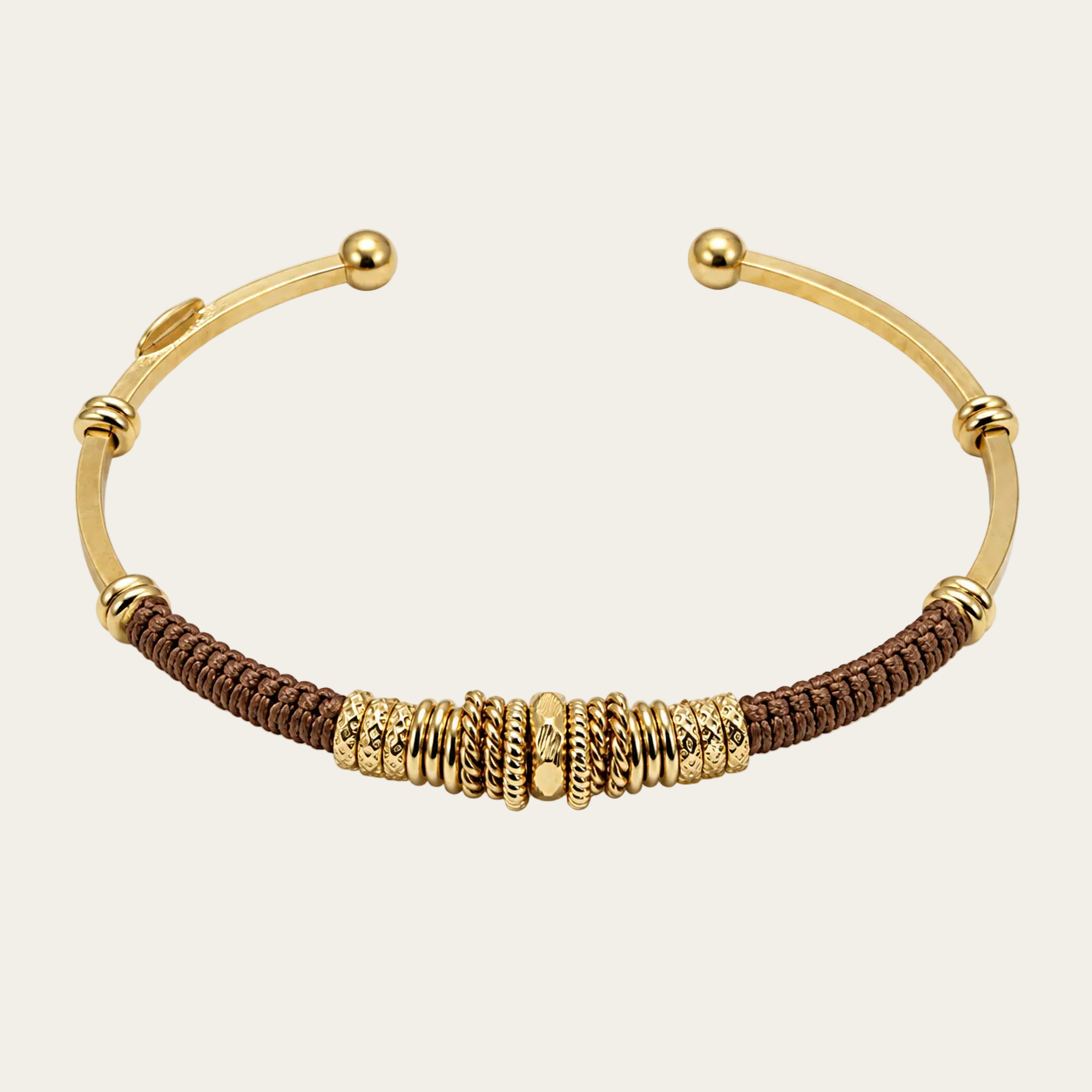 A gold-plated open cuff bracelet featuring a central brown braided cord section accented with textured gold spacers and polished gold ball end caps, shown on a clean white background.