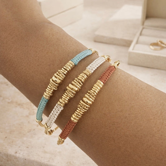 Three threaded gold bracelets on a wrist with a neutral background